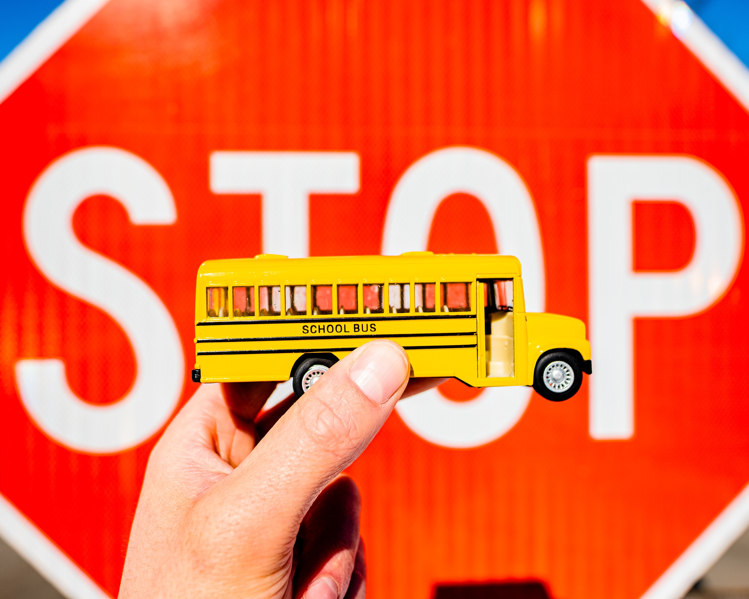 Maintenant un bus scolaire miniature devant un panneau STOP, illustrant la sécurité du transport scolaire